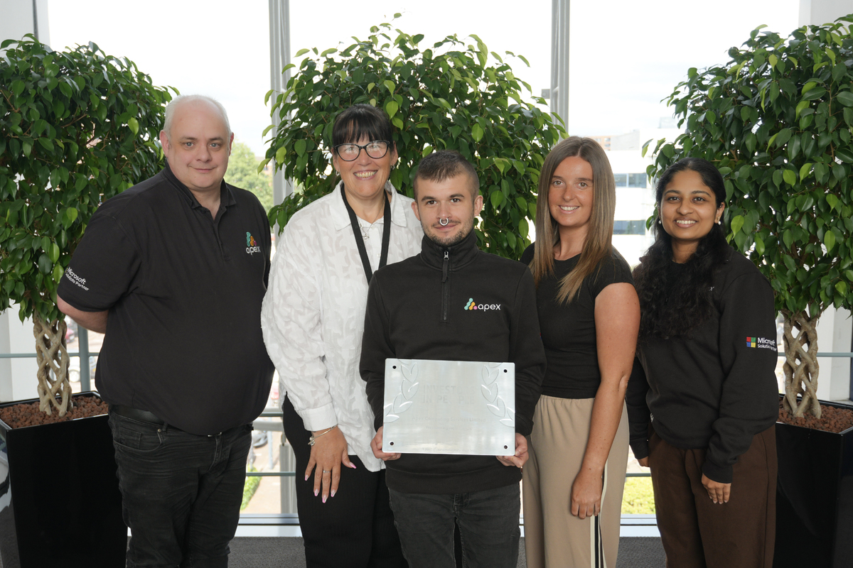 Five Apex team members stood in front of three round bushes, smiling to the camera. The middle employee is holding a platinum plaque for Investors in People Platinum accreditation