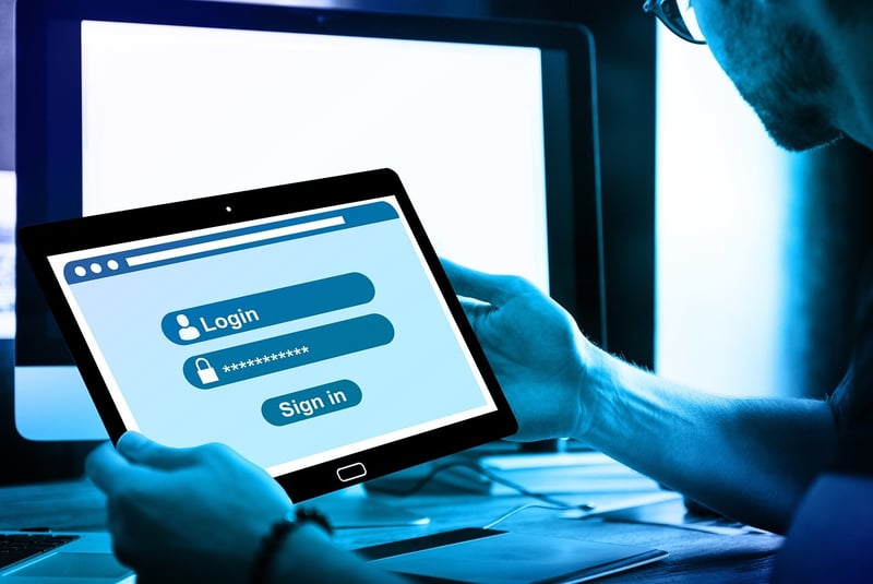 a man holding a tablet showing a login screen in front of a laptop computer